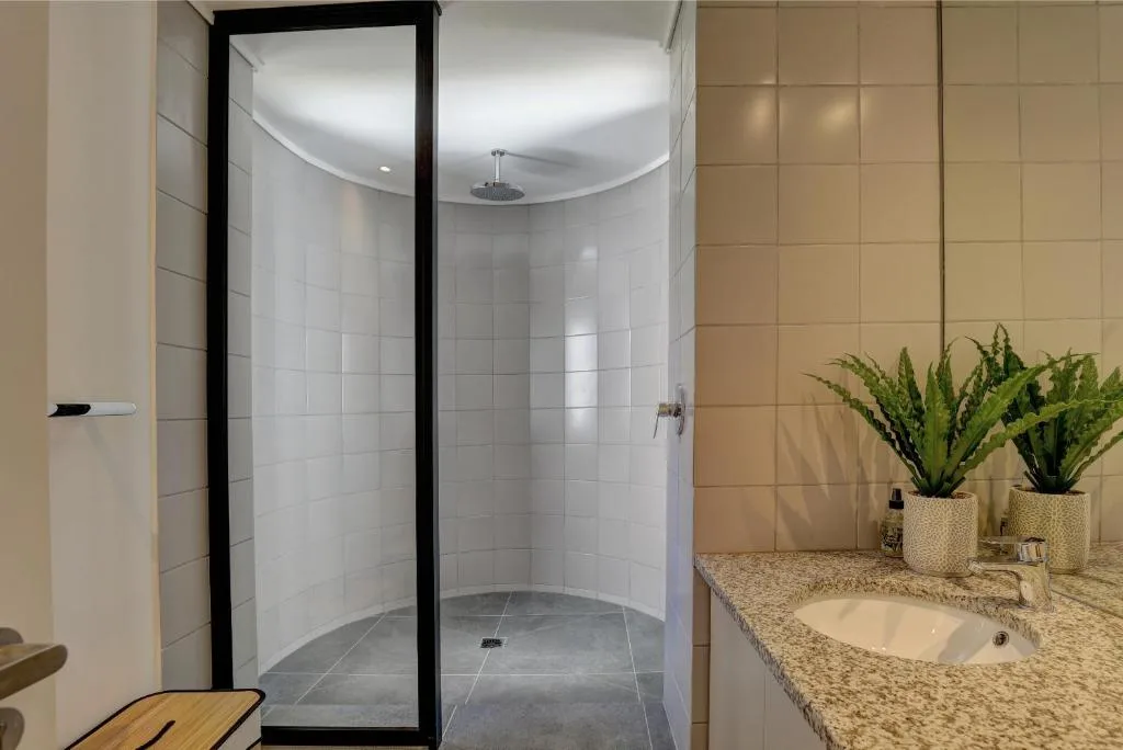 Modern bathroom with curved walk-in shower, granite countertop, and potted plants