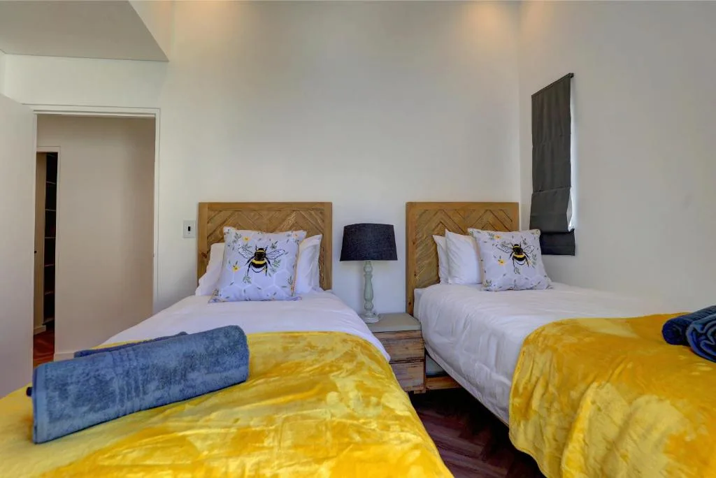 Twin bedroom with wooden headboards, bee-patterned pillows, yellow throws