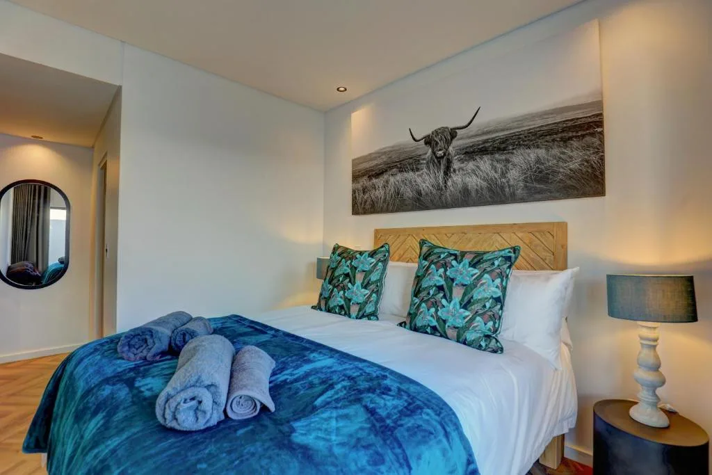Bright bedroom with queen bed, decorative pillows, rolled towels, and artwork
