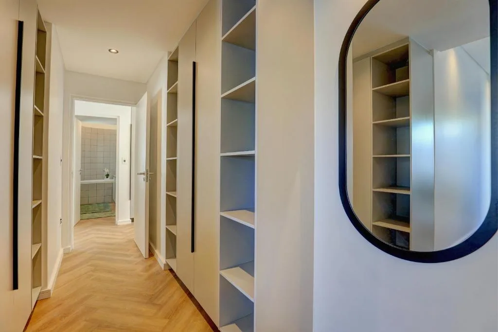 Modern hallway with built-in shelving, herringbone flooring, and circular mirror