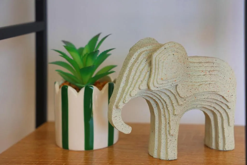 Decorative elephant sculpture and striped plant pot on wooden shelf
