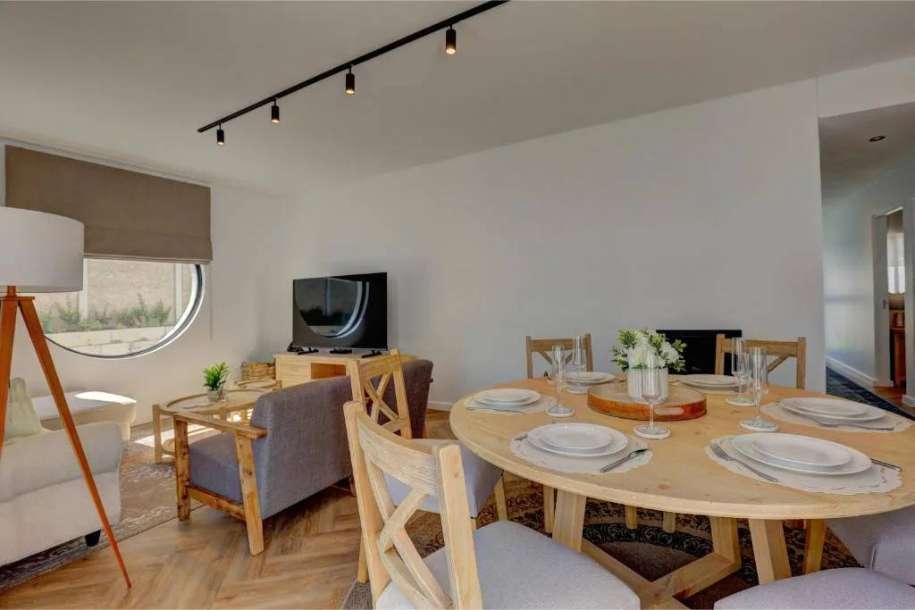 Modern dining area with wooden oval table, place settings, and lounge in background