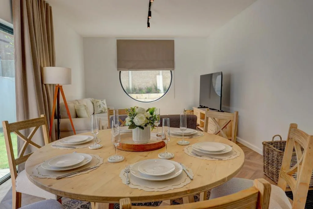 Round wooden dining table set for six with white place settings and fresh flowers