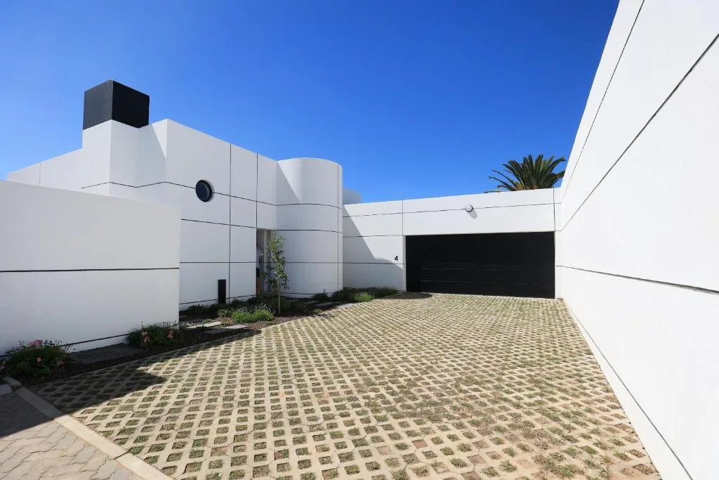 Modern white residence with black garage door and paved driveway
