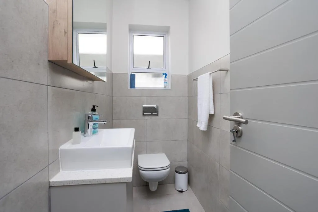 Modern bathroom with white basin, toilet, tiled walls, and window