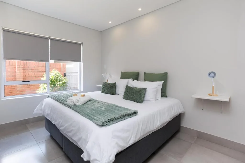 Modern bedroom with queen bed, green pillows, white linens, and natural light from windows