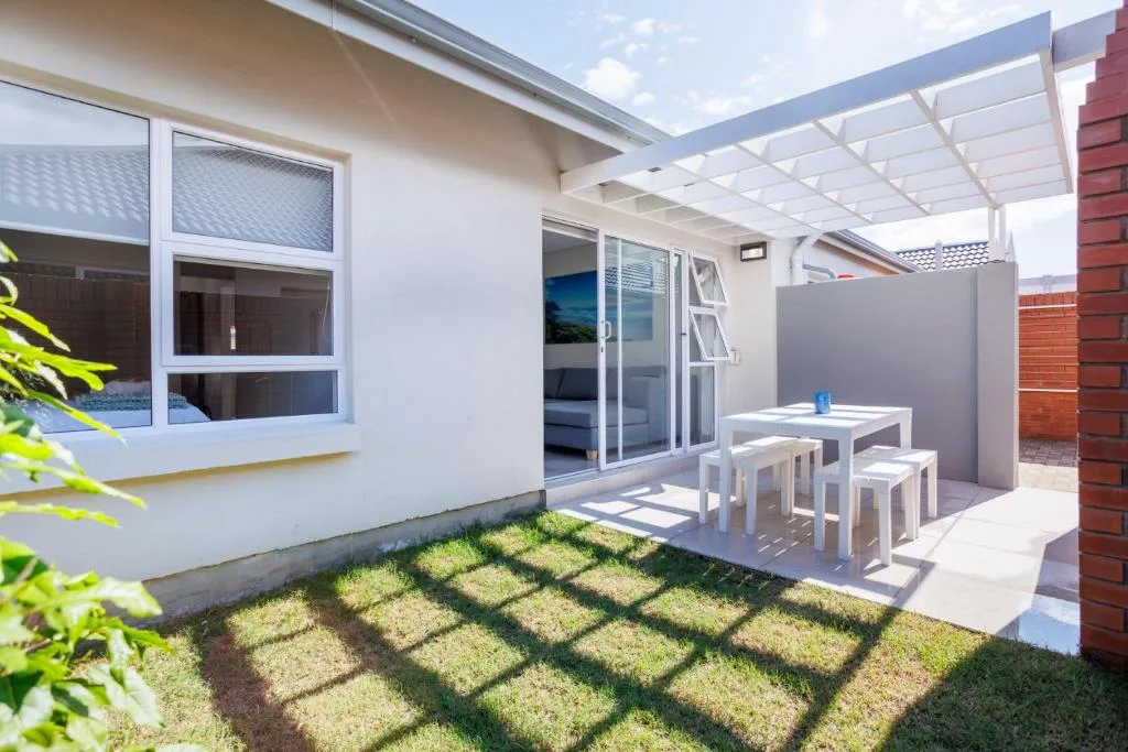 Contemporary patio with white pergola, dining table, and stools overlooking manicured garden
