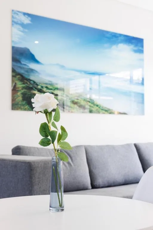 White rose in glass vase on table with mountain artwork