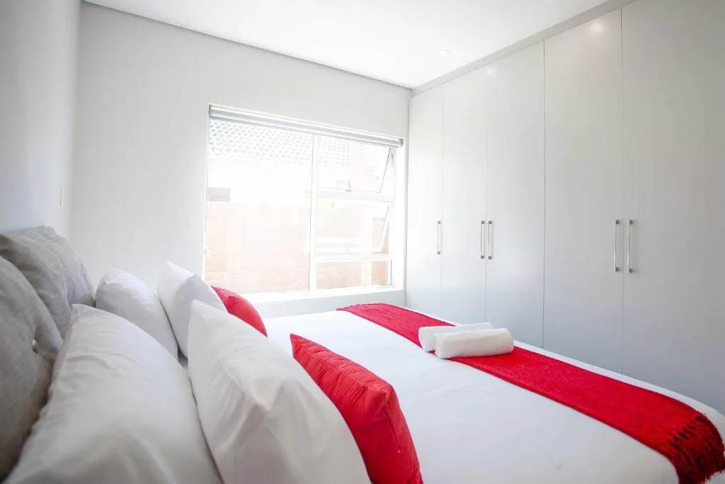 Bright modern bedroom with twin beds, red accents, built-in wardrobes