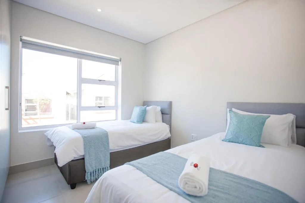 Bright bedroom with two beds, turquoise accents, and large windows overlooking garden.