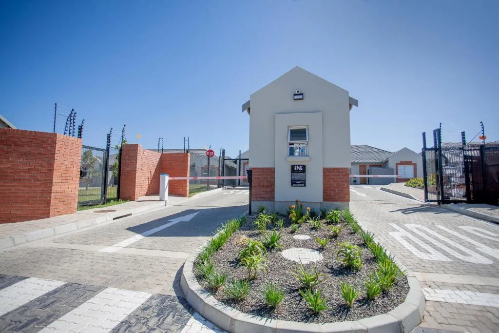 Modern white gatehouse with red brick entrance walls and landscaped garden bed