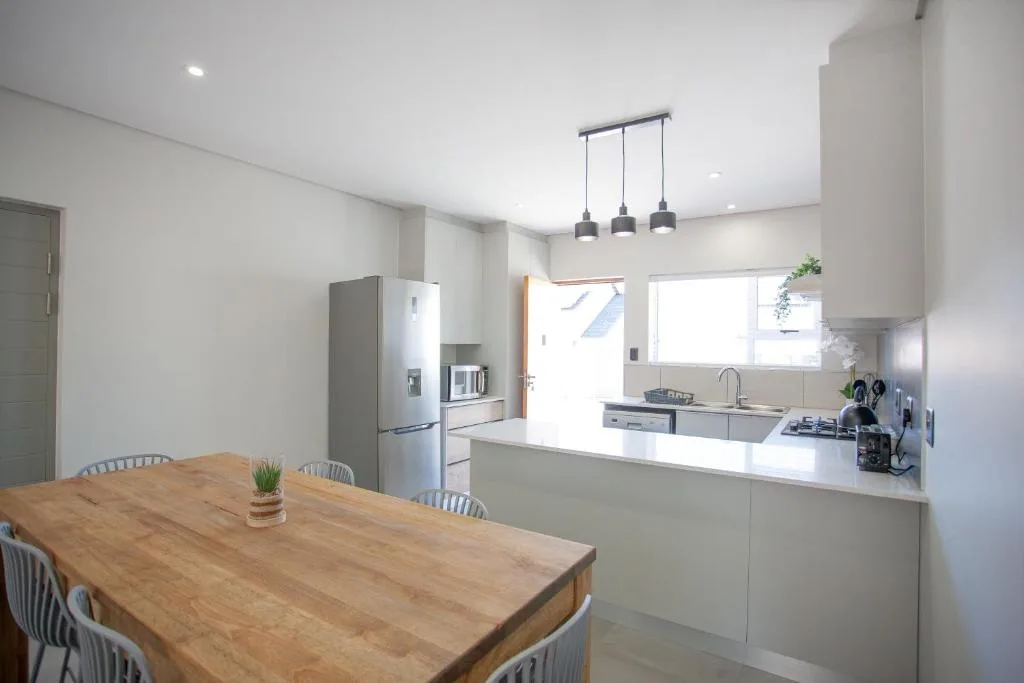 Modern open-plan kitchen with white cabinetry, stainless steel appliances, and dining table