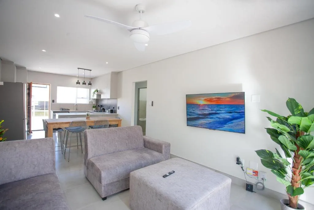 Modern lounge with grey sofa, ottoman, sunset artwork, and open-plan kitchen beyond