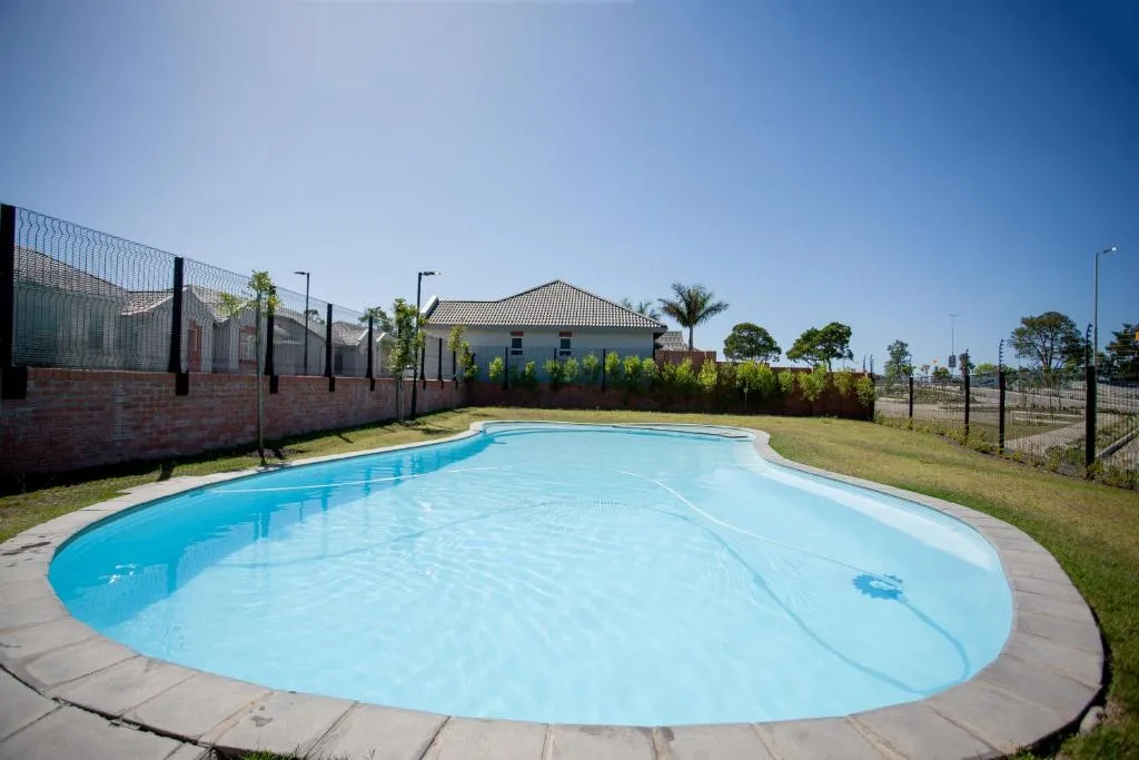 Bright blue oval swimming pool with concrete surround and fenced property