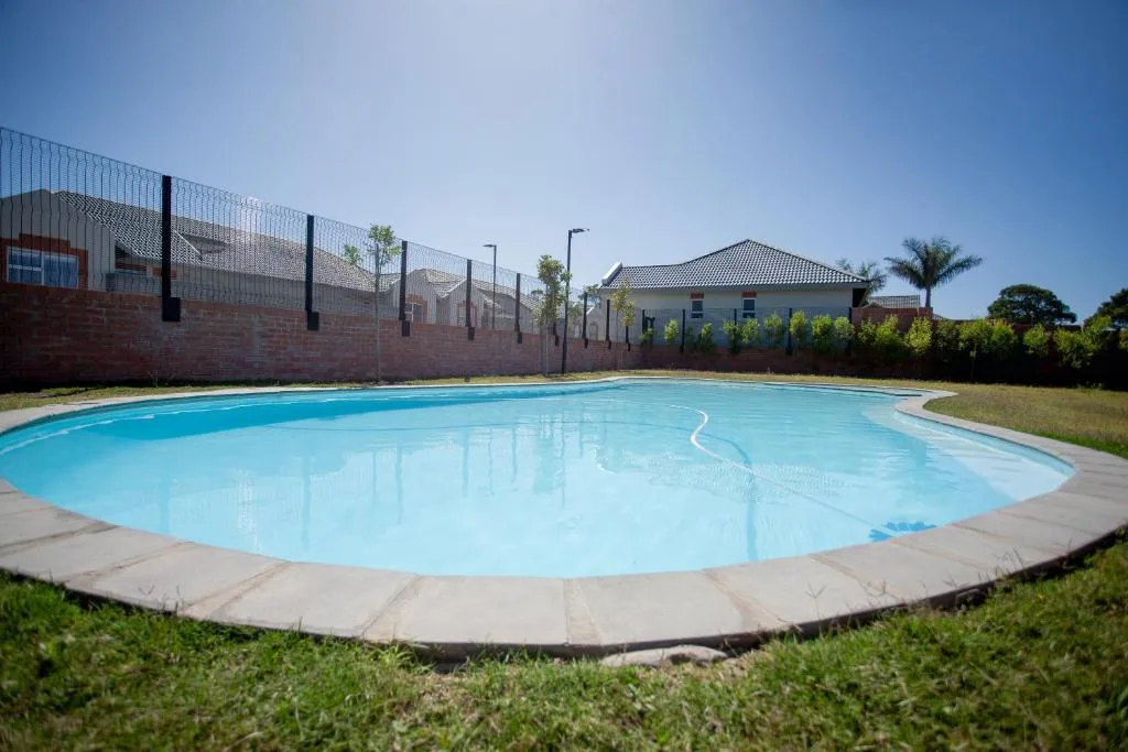 Large turquoise swimming pool with concrete surround and safety fencing