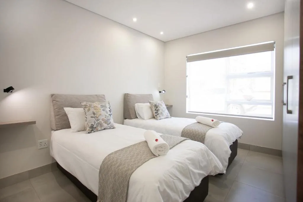Modern bedroom with two single beds, neutral bedding, and bright windows