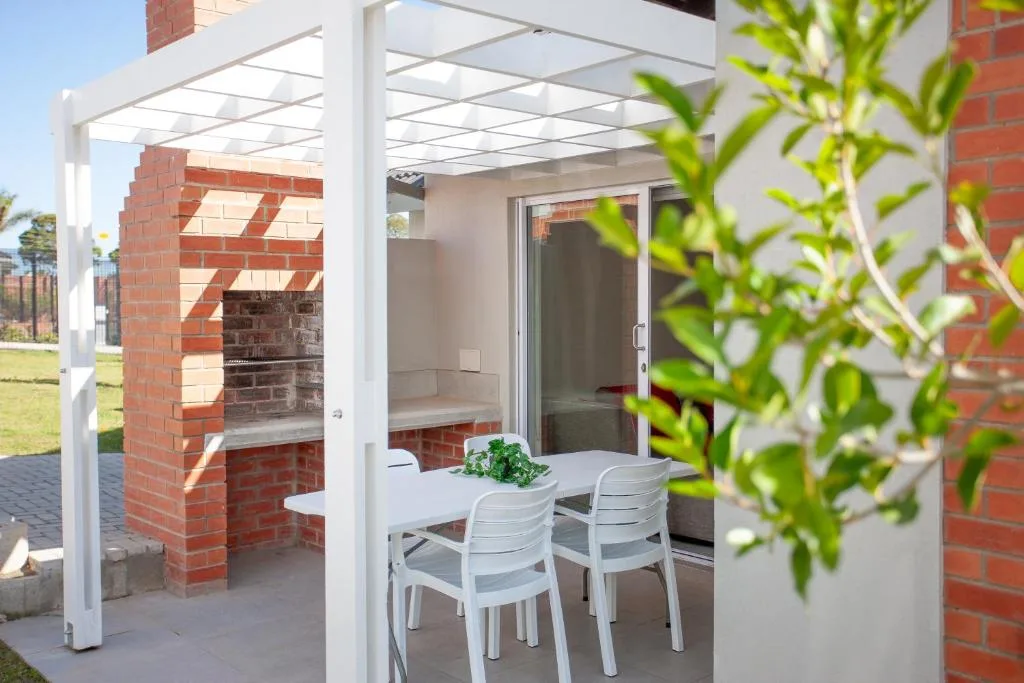 Modern pergola-covered patio with dining table and white chairs overlooking garden