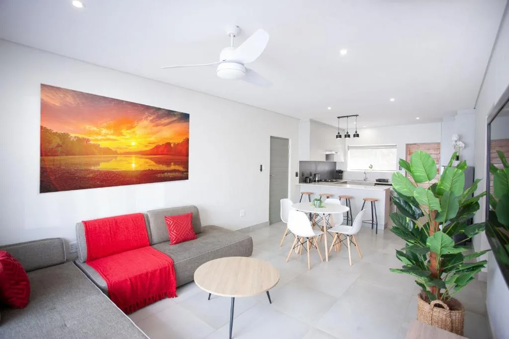Modern lounge with grey sofa, red accents, sunset artwork, and open-plan kitchen beyond