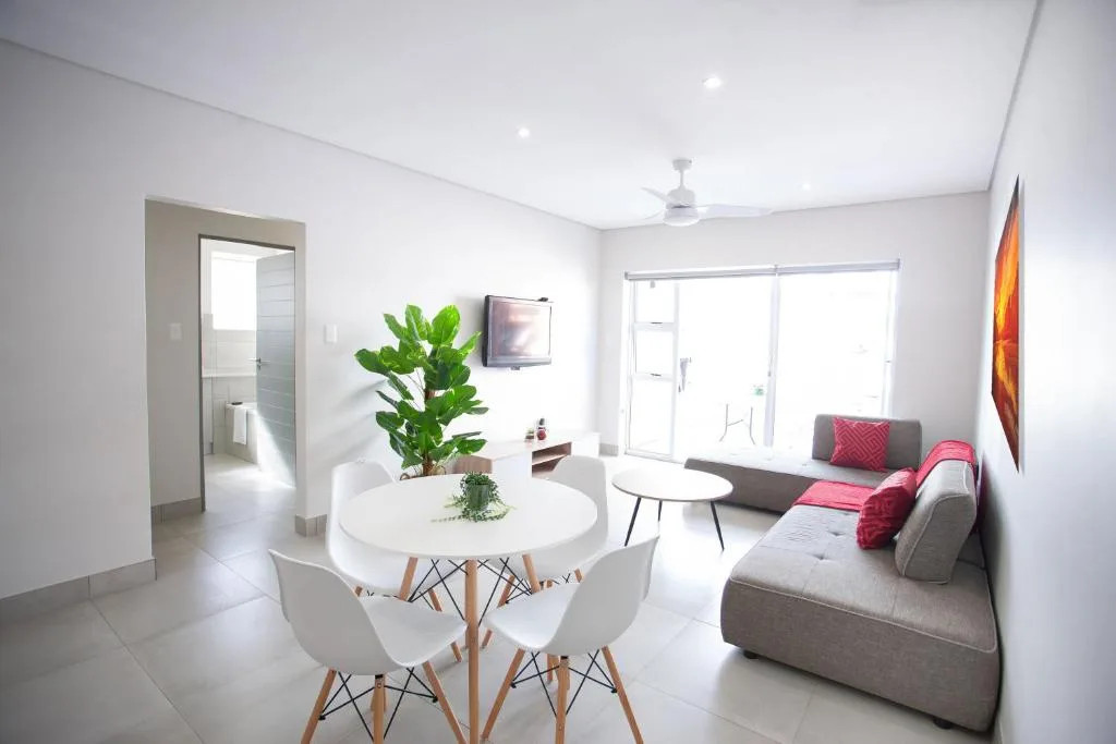 Modern lounge with gray sofa, pink accents, and dining area beyond