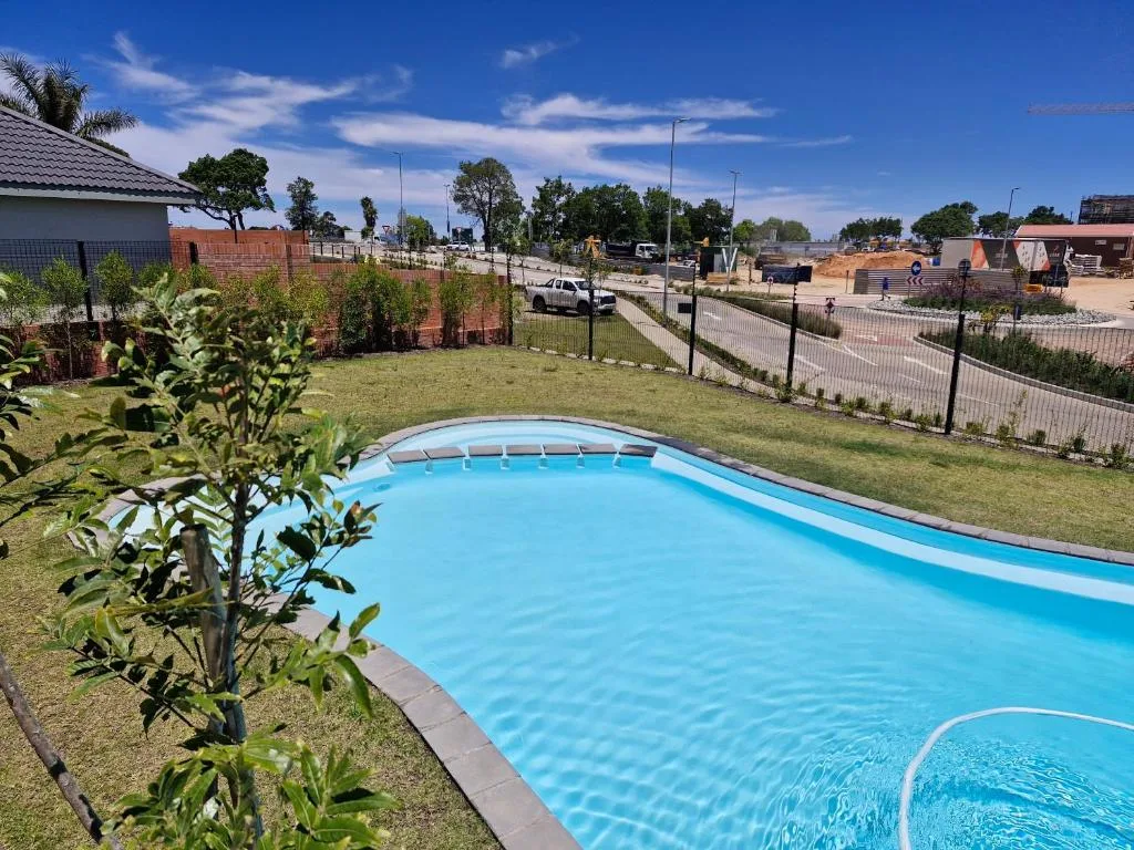 Bright blue swimming pool in manicured garden with fencing and clear sky