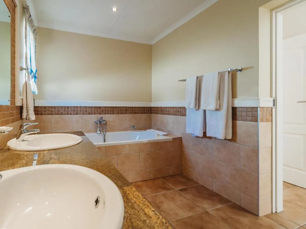 Spacious bathroom with dual sinks, soaking tub, and terracotta tile accents