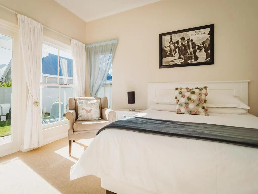 Bright bedroom with queen bed, armchair by windows overlooking garden