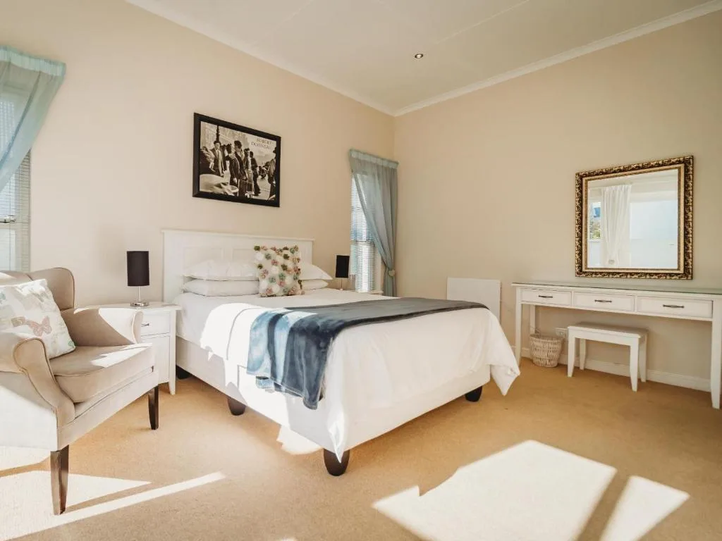 Bright bedroom with white bed, armchair, vanity desk, and natural light