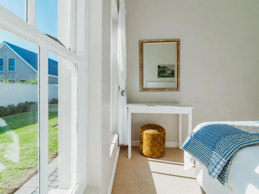 Bright bedroom with blue bedding, white fireplace, and garden views through glass doors
