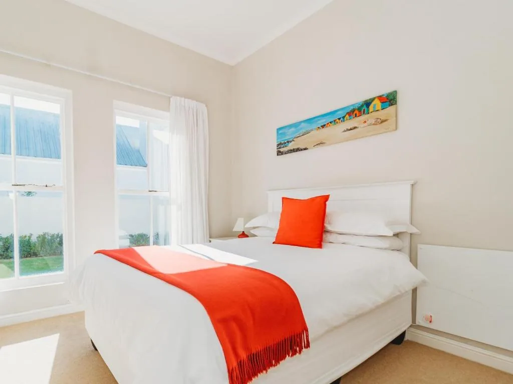 Bright bedroom with white bed, orange accents, and garden views