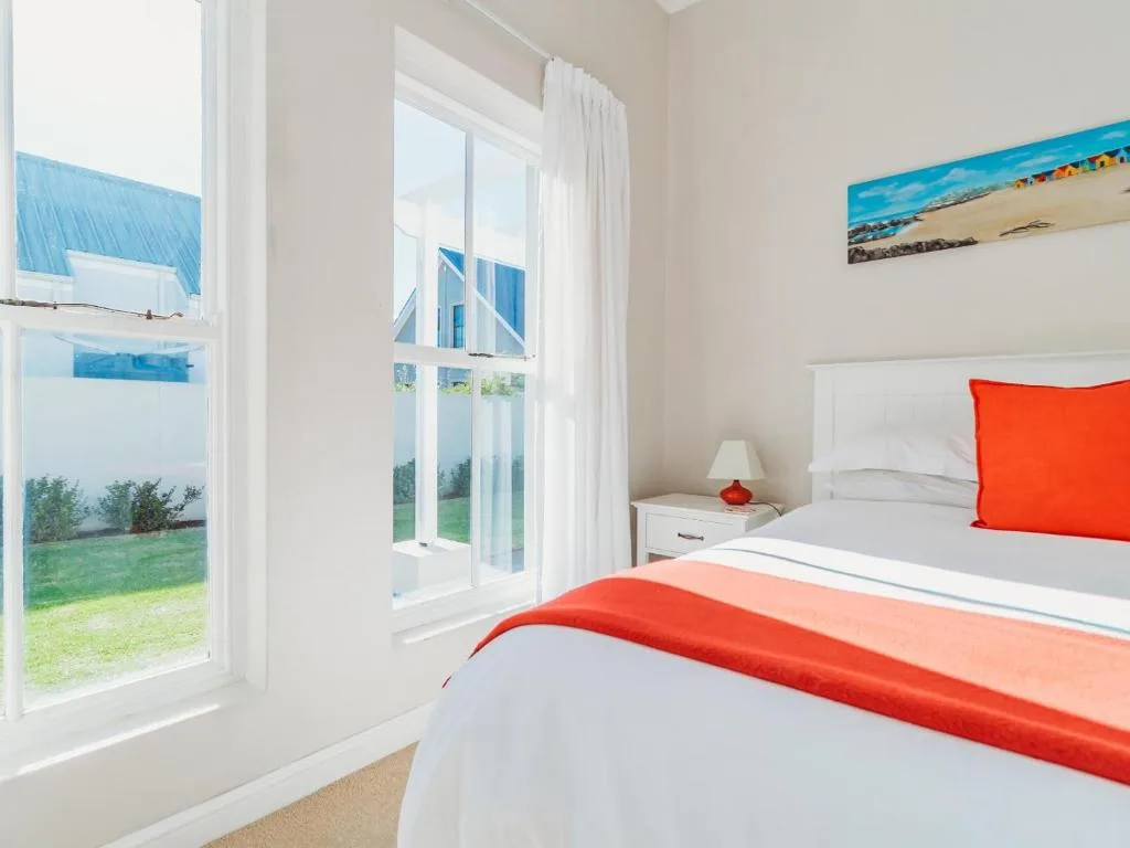 Bright bedroom with red accents, white bedding, garden views through French doors