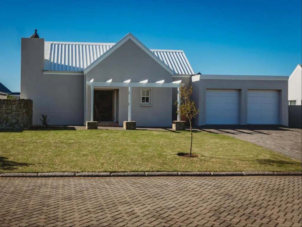 Modern gray cottage with white trim and blue garage doors on landscaped grounds