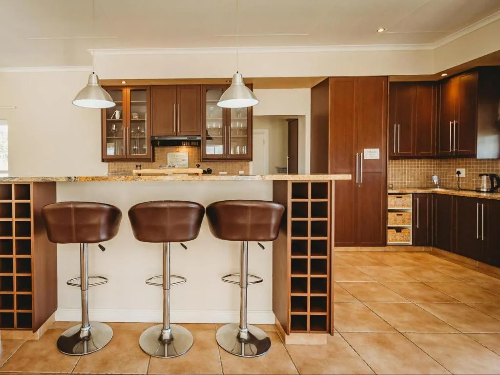 Modern kitchen with wooden cabinetry, granite countertop, and three brown leather bar stools