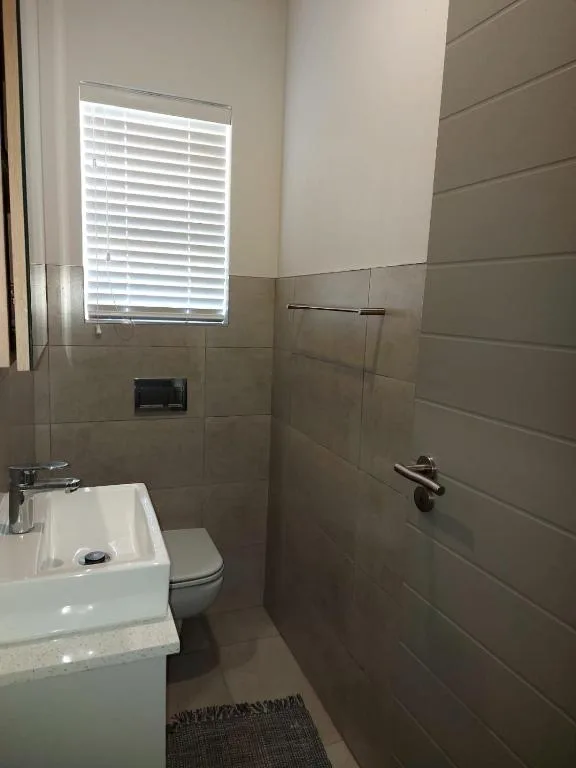 Modern bathroom with toilet, sink, tiled shower area, and window