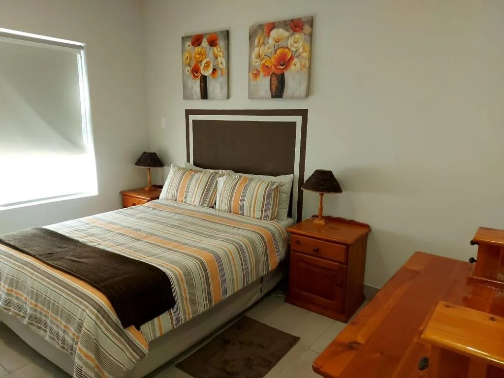 Bright bedroom with striped bedding, wooden nightstands, and floral wall art