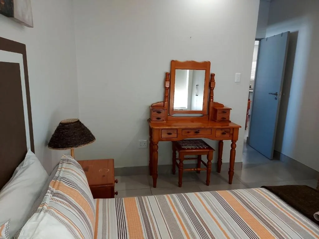 Bedroom with striped bedding, wooden vanity dresser, and bedside lamp