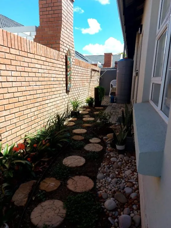 Brick courtyard with stepping stones, potted plants, and manicured garden beds