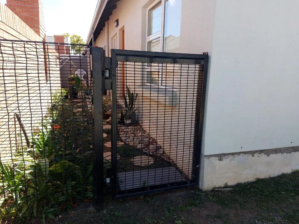 Black metal gate entrance with garden plants and property facade