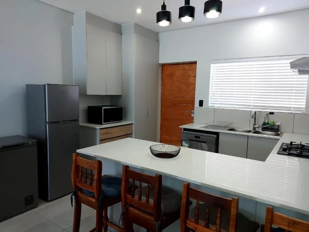 Modern kitchen with white counters, stainless appliances, dining island, and wooden chairs