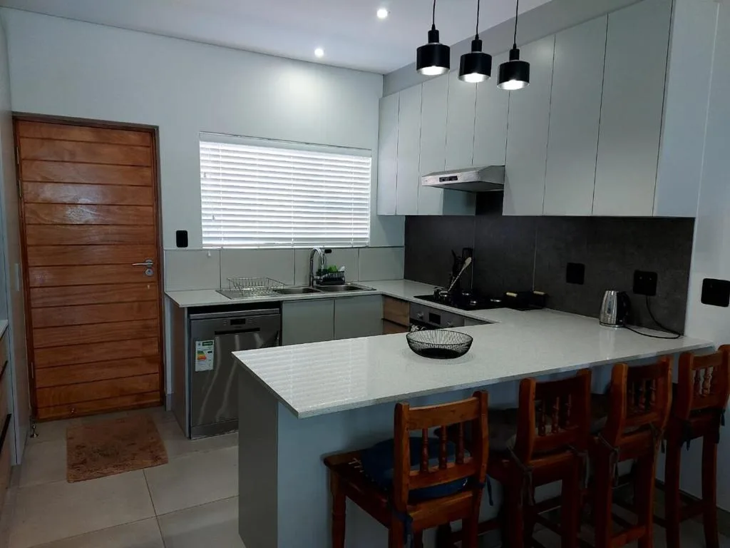Modern kitchen with white cabinetry, black backsplash, island counter, and wooden dining chairs