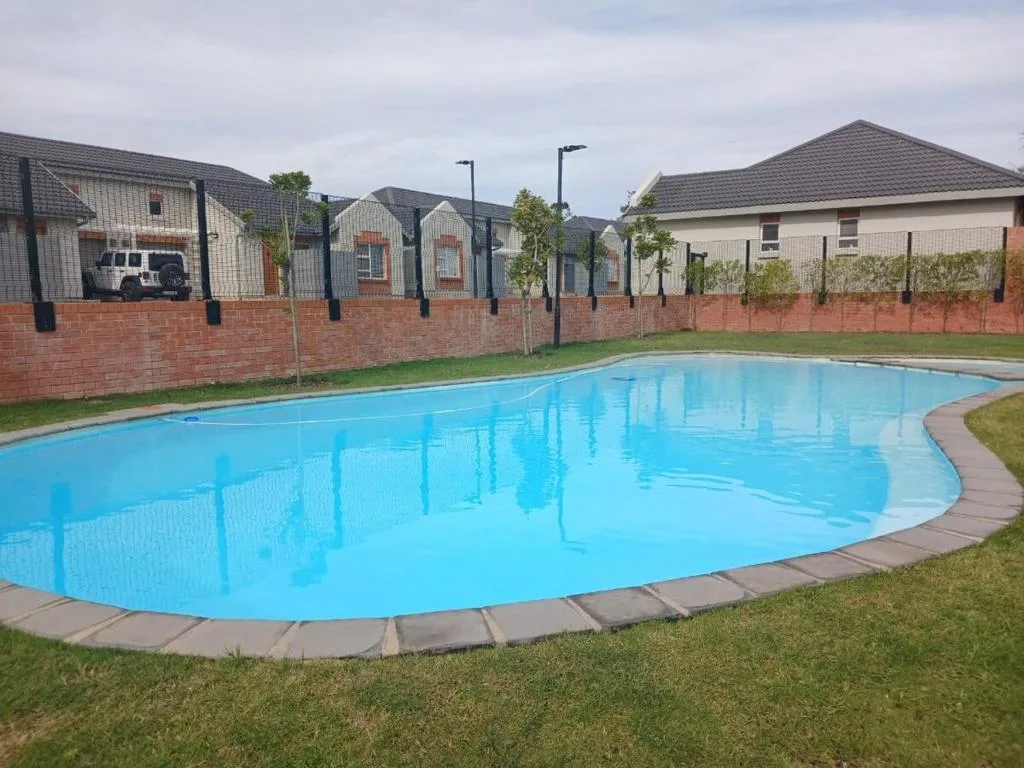 Bright blue oval swimming pool with manicured lawn and fenced property buildings