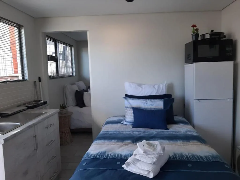 Compact bedroom with blue striped bedding, kitchenette, and white refrigerator