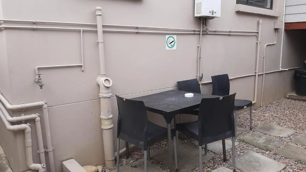 Outdoor patio area with black dining table and four chairs against pink wall