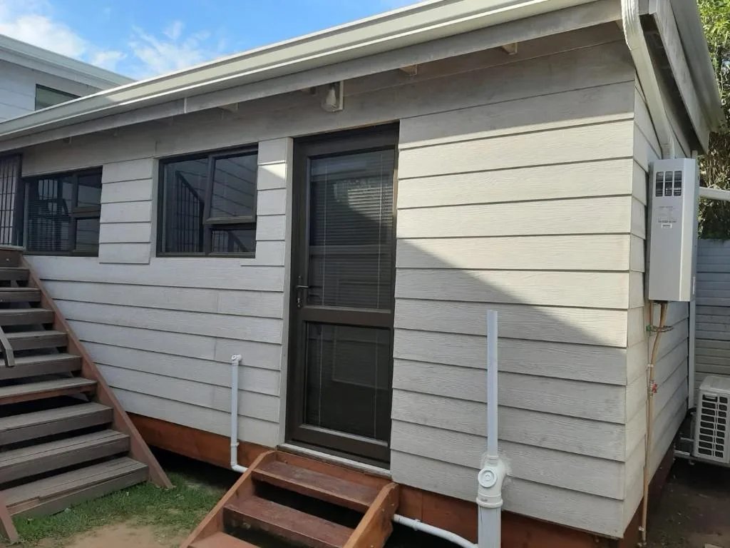 Modern white weatherboard cottage with dark windows and wooden entrance steps