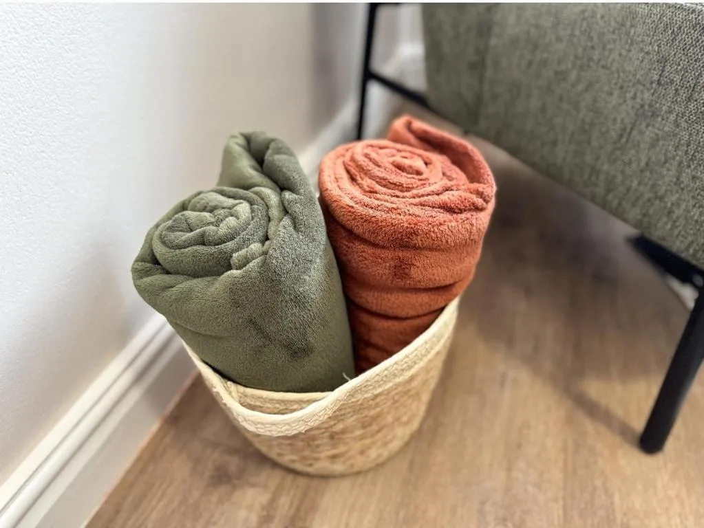 Rolled green and terracotta towels neatly arranged in woven basket