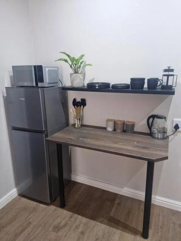 Modern kitchenette with grey fridge, wooden counter, and open shelving displaying dishes