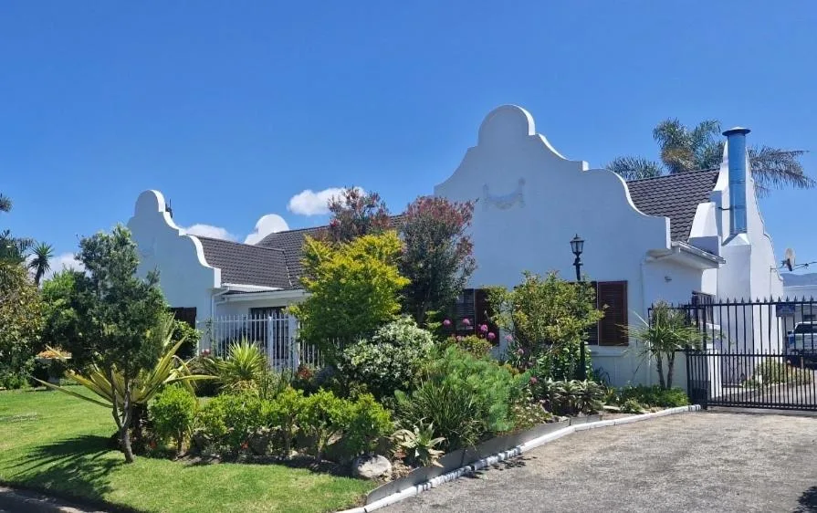 White Cape Dutch style house with manicured gardens and black iron gates