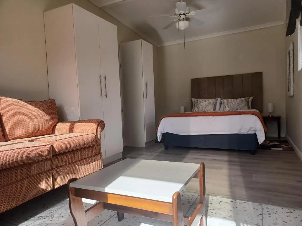 Spacious bedroom with queen bed, orange sofa, and white wardrobes