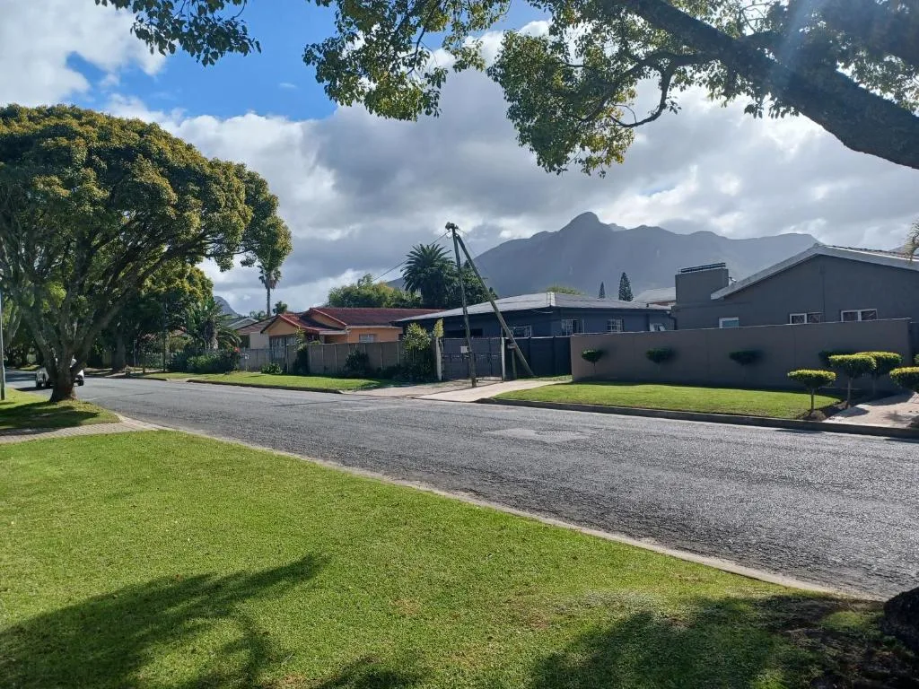 Modern cottage with manicured gardens and mountain views beyond tree-lined driveway