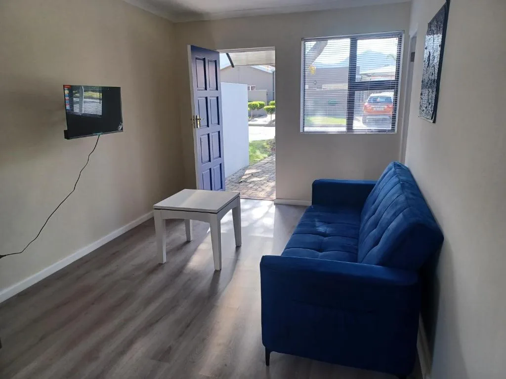 Bright lounge with blue sofa, wall-mounted TV, and open entrance doors