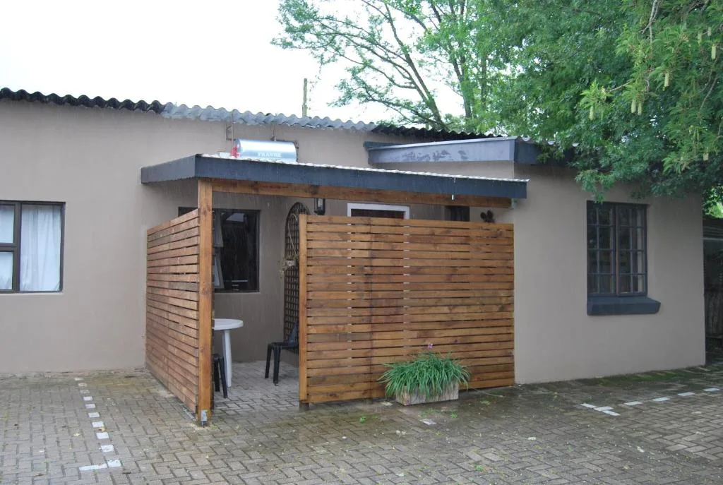 Cottage entrance with wooden deck and brick paving, tree-shaded property